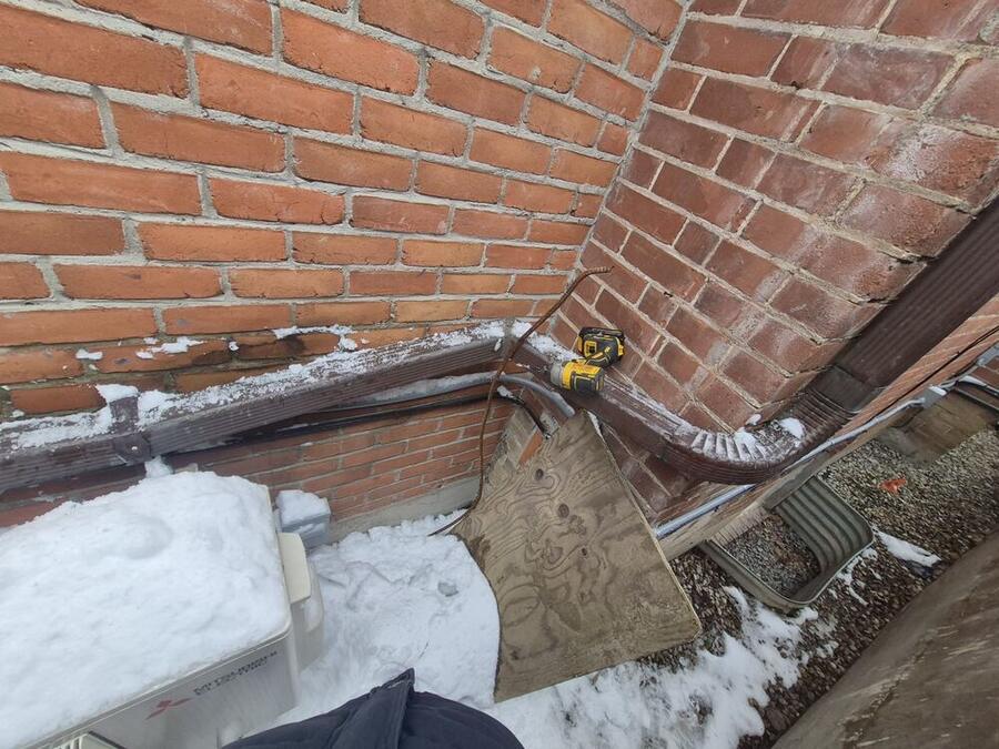 Worn horizontal downspout and elbow being replaced in winter