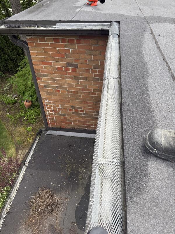 Gutter guard reinstalled after cleaning next to a brick chimney